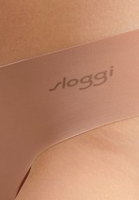 Culotte en tissu nude avec une ceinture élastique lisse portant discrètement le nom de la marque "sloggi" en relief. Le matériau est extensible et sans coutures.