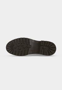 Semelle d'une botte noire avec des motifs de bande de roulement profonds et robustes, comprenant des rainures en forme de croix et droites pour une meilleure adhérence et durabilité.