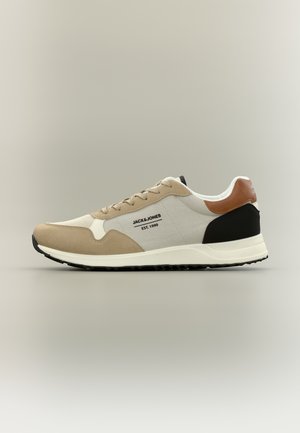 Beige, witte, zwarte en bruine sneaker met veterontwerp, rubberen zool en "JACK & JONES EST. 1990" logo aan de zijkant.