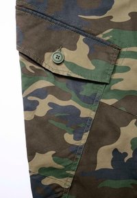 Telas de camuflaje con una mezcla de patrones verdes, marrones y negros. Incluye un bolsillo con solapa y un botón verde. Textura suave.
