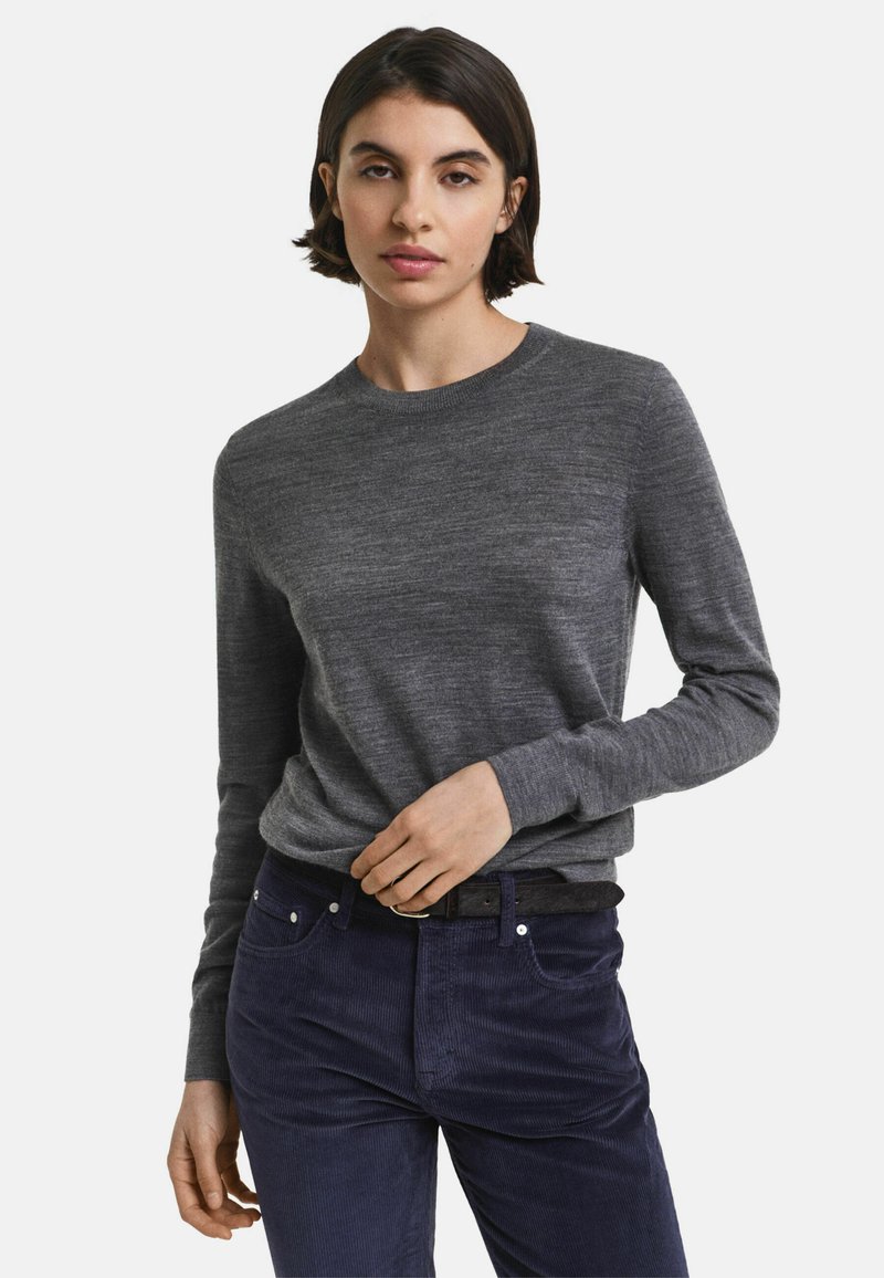 Pullover grigio a maniche lunghe con scollo rotondo, realizzato in tessuto morbido. Il modello indossa pantaloni in velluto a coste blu navy con una cintura nera.