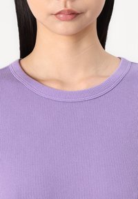 Maglione viola a coste con scollatura rotonda e tessuto testurizzato, che mette in evidenza righe verticali e una finitura morbida e liscia.