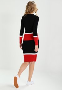 Strickkleid mit taillierter Passform in schwarz, rot und weiß gestreift. Lange Ärmel, knielanger Rock, kombiniert mit weißen Sneakern.