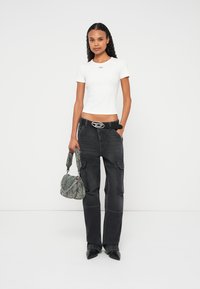 Top cropped branco de manga curta, calças cargo cinzento escuro com bolsos, cinto preto com ferragens prateadas, mala texturada cinzenta e sapatos pretos apontados.