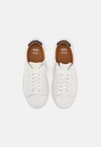 Hvide lædersneakers med snørebåndsdesign, sidelukning med lynlås og brun indersål. Branding synlig på indersålen og hælen.