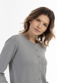 Szürke kardigán kerek nyakkivágással, elöl gombos záródással, puha textúrával és hosszú ujjakkal. Négy kerek gombbal és testhezálló szabással rendelkezik.