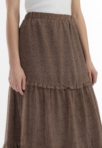 Gonna a strati floreale marrone realizzata in un tessuto leggero con vita elastica e dettagli arricciati alle cuciture.