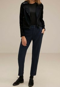 Svart faux läderbikerjacka över en figurnära svart topp, parat med marinblå tapered byxor, uppvikta ärmar och svarta snörskor.