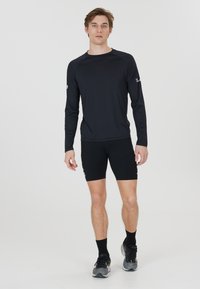 Black long-sleeve athletic shirt and fitted black shorts. The shirt features a smooth texture and subtle logo detail on the sleeve.