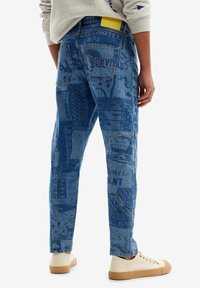 Blue denim jeans with a relaxed fit, featuring varied textures and printed patterns. Includes five pockets and contrasting stitching details.