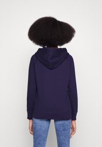 Felpa della marina con cappuccio regolabile, polsini a coste e un fit rilassato. Abbinata a jeans azzurri, che mostrano dettagli di cucitura ben definiti.