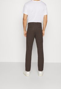 Bruna rutiga byxor med skräddarsydd passform, utrustade med bakfickor och en slät textur, kombinerade med en enfärgad vit t-shirt och vita sneakers.