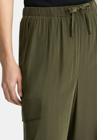 Pantalones ligeros de color verde oliva con una cintura elástica, una cinta de tela en la cintura y un bolsillo lateral. Textura suave con un ligero brillo.