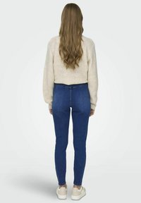 Suéter de punto cable en color beige claro combinado con jeans de tiro alto en azul oscuro. Los jeans son ajustados, con costuras sutiles y dobladillos a la altura del tobillo.
