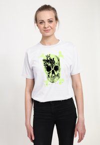 Bílá bavlněná tričko s černou a neonově zelenou grafikou lebky s kostmi. Jednoduchý střih s kulatým výstřihem a krátkými rukávy.