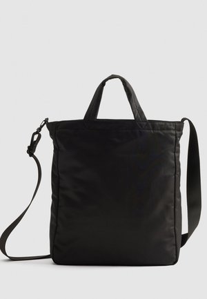 Sac cabas rectangulaire noir avec poignées courtes et longue bandoulière amovible sur fond uni.