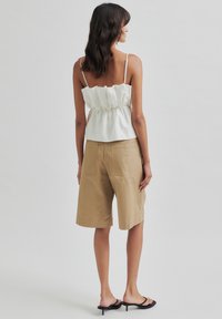 Top scurt alb, cu volane și bretele subțiri, asortat cu pantaloni scurți bej, până la genunchi. Modelul poartă sandale negre, cu toc și vârf deschis.