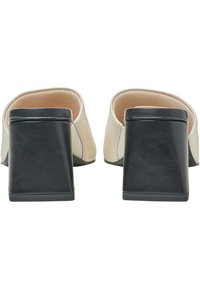 Scarpe slip-on in pelle color crema con un ampio tacco a blocco nero e rivestimento interno liscio, caratterizzate da un design minimalista.