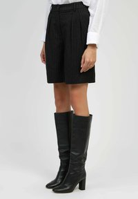 Shorts ajustés à rayures noires avec une coupe décontractée, associés à des bottes en cuir noires montantes et ajustées avec un talon carré.