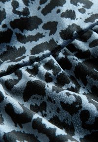 Tkanina s leopardím vzorom v modro-čiernej farbe, s hladkou textúrou a jemným leskom, predvádzajúca mäkké, splývavé záhyby.