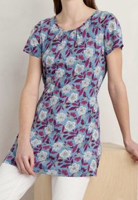 Bloemrijke tuniek top in het blauw met korte mouwen. Heeft witte en bordeauxrode patronen van bloemen en bladeren, een ronde halslijn en een geraffineerde detail.