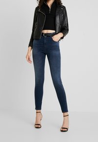 Tmavě modré džínové skinny džíny s vysokým pasem, kombinované s černým krátkým žebrovaným topem a černou koženou bundou s detaily na zipu a přezce.