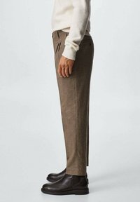 Ruske ručno tkanih hlača s kariranim uzorkom, ravnog kroja, s prednjim nabora i kombiniranih s tamnim kožnim čizmama.