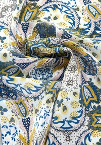 Tissu à motifs présentant des designs floraux et paisley complexes en bleu, jaune et rose sur un fond clair. Texture douce et lisse.