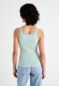 Top in maglia a coste verde menta con bordino in pizzo sulle spalline, design aderente. Abbinato a jeans di jeans azzurri, visto da dietro.