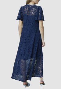 Mørkeblå maxikjole i blonde med korte udvidede ærmer, der viser et blomsterdesign og en gennemsigtig nederste sektion, der har en nøglehulslukning bagpå.