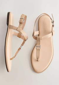 Beige leather sandals with flat soles, ankle straps, and silver hardware accents. Features minimalist design and smooth texture.