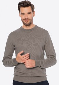 Szary teksturowany sweter z okrągłym dekoltem i ściągaczami na mankietach. Ręce modelki delikatnie spoczywają na przodzie, ukazując dopasowanie odzieży.