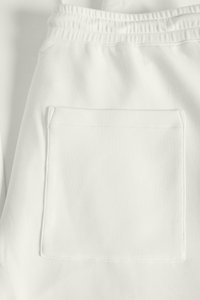 Bele trenirke z elastičnim pasom, gladko teksturo in kvadratnim žepom na hrbtni strani. Nežen logotip na pasu.