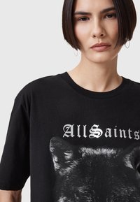 Mustat puuvillapaidat, joissa on susi grafiikka ja "AllSaints" teksti metallinhohtoisena hopeana. Klassinen pyöreä kaula-aukko ja lyhyet hihat.