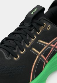 Scarpa sportiva nera con superficie testurizzata, hardware dorato e suola verde. Presenta accenti colorati in arancione e rosa. Design con lacci.