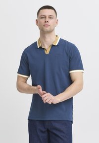 Mornarsko polo majica s kontrastnim rumenim ovratnikom in belimi robovi. Mehka bombažna tkanina, kratki rokavi in subtilno blagovno znamko na prsih.