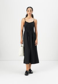 Vestito nero senza maniche con un busto aderente e una gonna fluida. Abbinato a una borsa bianca testurizzata e mocassini neri. Design semplice ed elegante.
