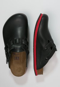 Schwarze Lederclogs mit strukturiertem Finish, ausgestattet mit zwei Schnallen und einem roten Akzent auf der Sohle. Kork-Innensohle und Gummi-Außensohle für Grip.
