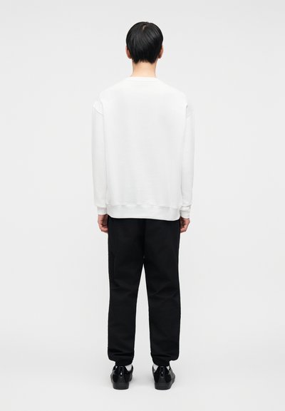 Λευκό φούτερ με στρογγυλή λαιμόκοψη και χαλαρούς ώμους, συνδυασμένο με μαύρο παντελόνι χαλαρής εφαρμογής με πλαϊνές τσέπες. Λείο ύφασμα.