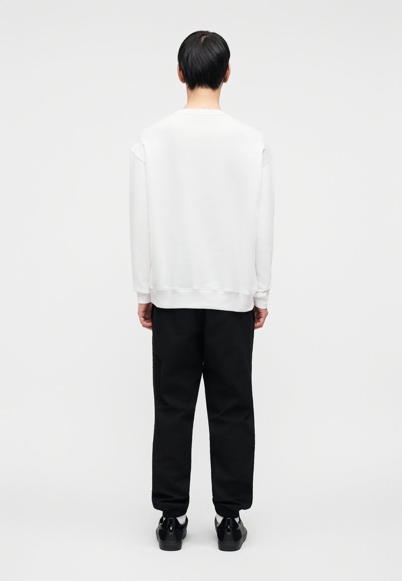 Sweat-shirt blanc à col rond et épaules tombantes, associé à un pantalon noir à coupe décontractée avec poches latérales. Texture lisse.