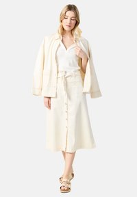 Kreemi puuvillane jakk, ribaga valge tipp ja pikk seelik, millel on nööpide eespool. Kantud beežide sandaalidega. Sile tekstuur, lõdva disainiga.