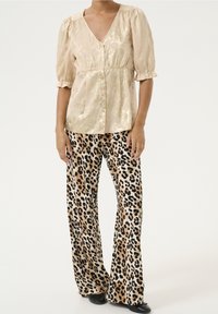 Blusa beige chiara con scollatura a V e maniche a palloncino, abbinata a pantaloni a gamba larga con stampa leopardata nei toni beige, nero e marrone.