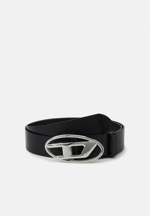 Cinto de couro preto com uma fivela oval prateada com um design recortado. A tira é lisa e ligeiramente texturizada.