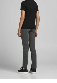 Schwarzes kurzärmeliges T-Shirt kombiniert mit grauen Slim-Fit-Sweatpants und schwarzen Sneakers. Die Hose hat eine glatte Stoffstruktur und einen elastischen Bund.