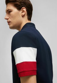 Maritimes Polohemd aus strukturiertem Stoff, mit kurzen Ärmeln in rot-weißem Streifenmuster. Klassisches Kragen-Design, taillierte Passform.