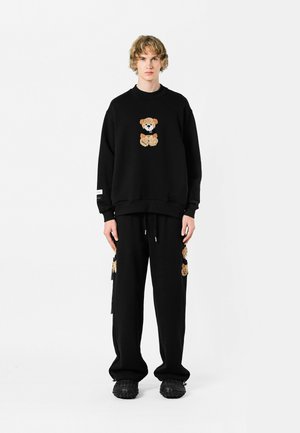 Conjunto de sudadera y pantalones negros con un diseño de oso de peluche en una tela texturizada. La sudadera tiene mangas largas, mientras que los pantalones tienen detalles en los bolsillos.