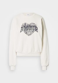 Κρεμ κοντή μπλούζα με μακριά μανίκια. Διακοσμείται με μεγάλο γραφικό σε σχήμα καρδιάς με λεοπάρ μοτίβο και τη λέξη «AMOUR» με έντονα μπλε γράμματα.