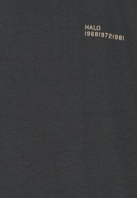 Czarna tkanina z beżowym napisem "HALO" i cyframi "1968 1972 1981" nadrukowanymi w pobliżu górnego prawego rogu.