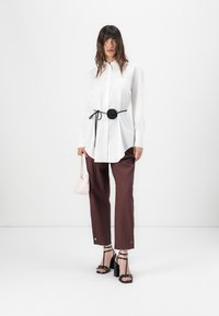 White button-up shirt with a black rose belt, paired with burgundy trousers and black strappy heels; holding a pink handbag.