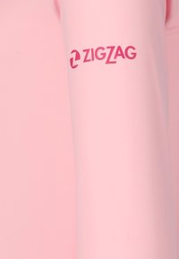 Lyserød langærmet skjorte med en glat tekstur og rund halsudskæring; har et pink "ZIGZAG" logo på ærmet.